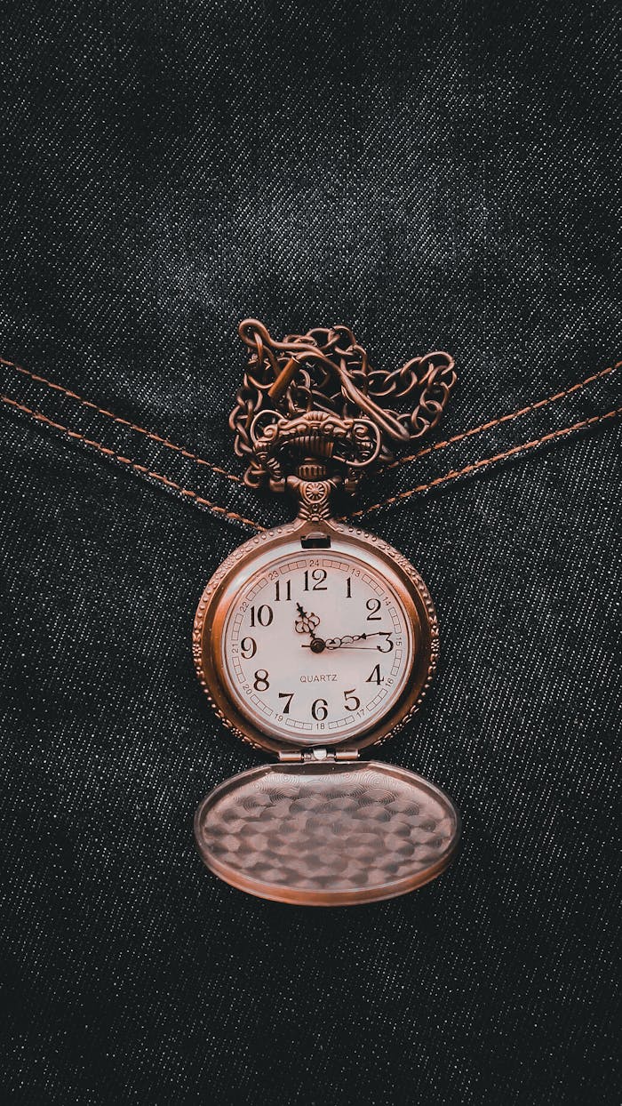 Close-up of an elegant vintage pocket watch with a chain on a textured denim background.